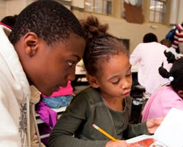 Two children looking at a paper, one holding a pencil