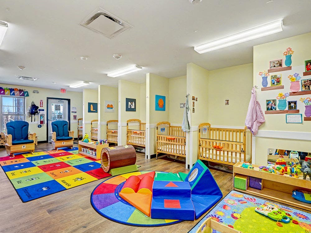 A childcare classroom with cribs, playmats, toys, and small chairs