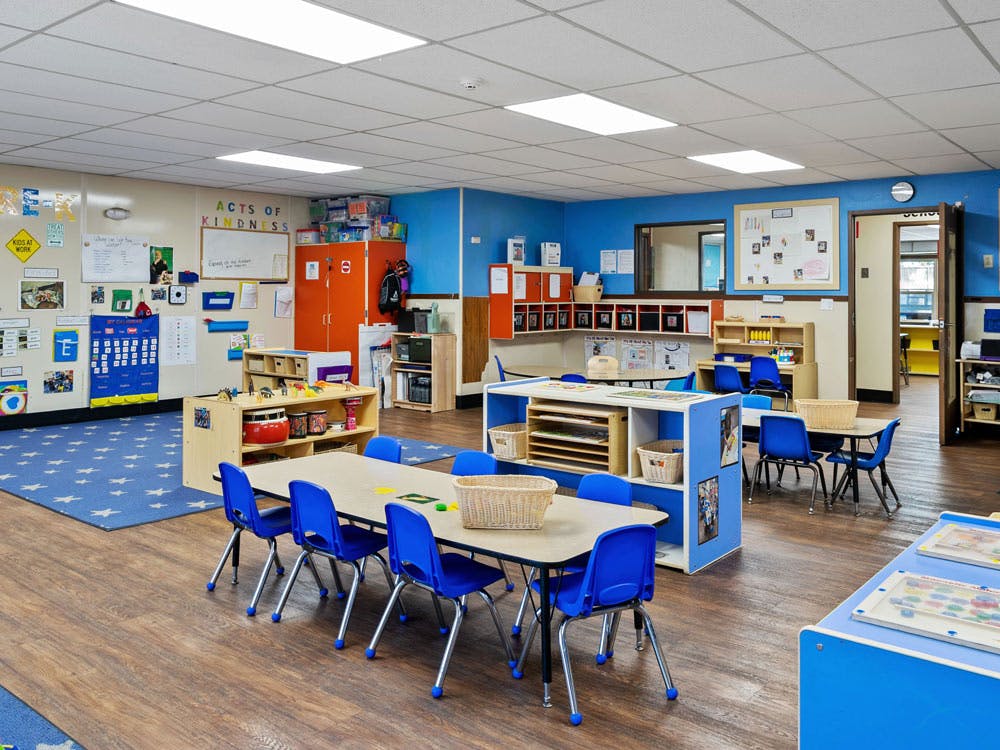 Empty classroom with small tables and chairs, and learning materials on shelves