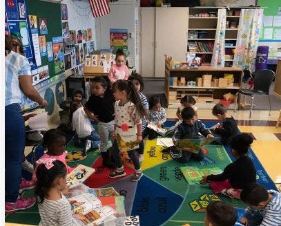 Children in a classroom, some sitting on a rug and some standing
