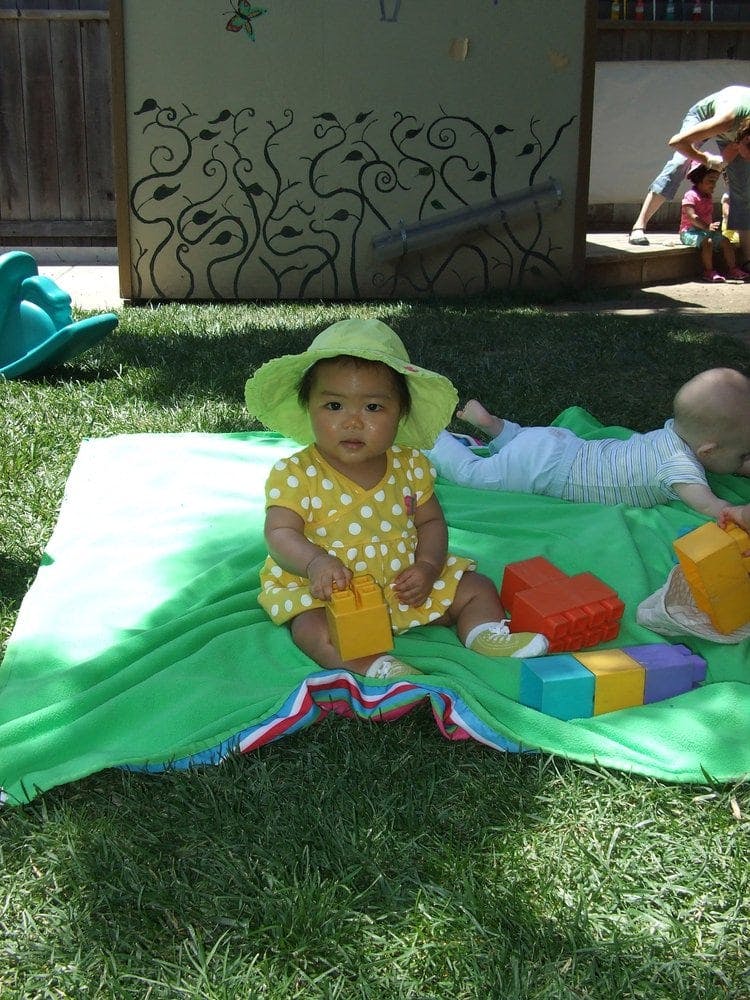 Child in a sun hat sitting on a blanket with toys