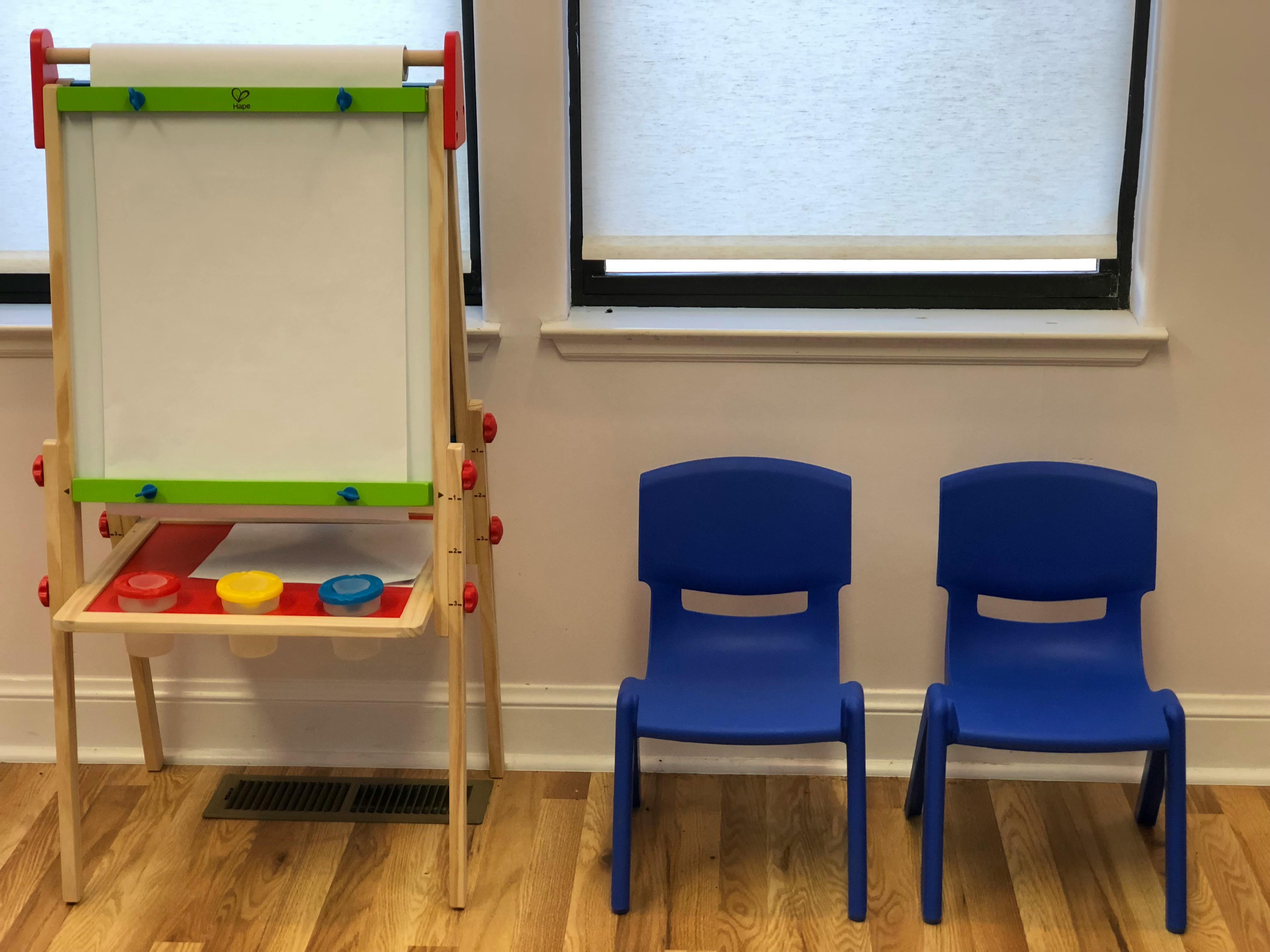 Easel with paint cups and two blue chairs in a room