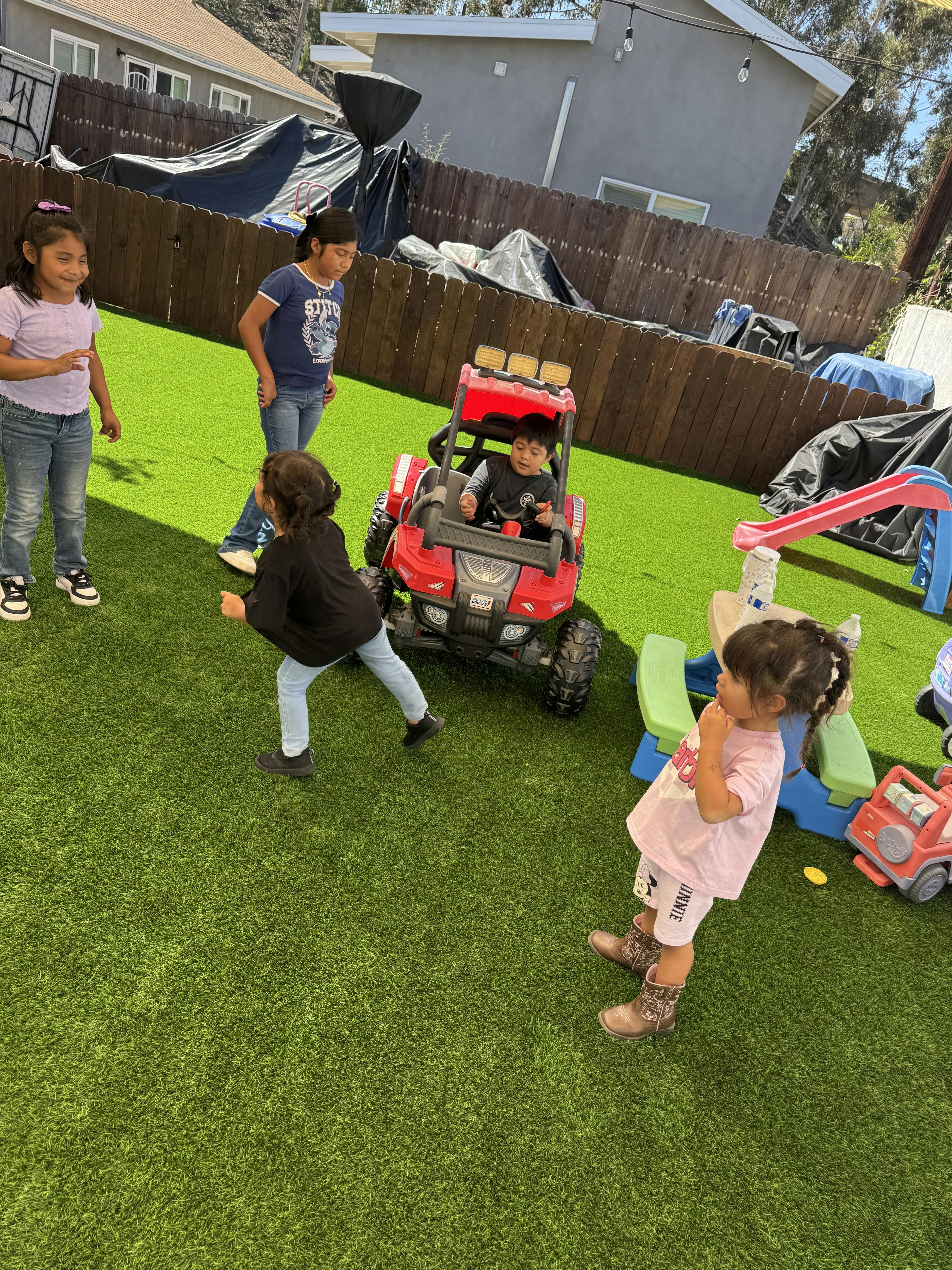 Children playing outdoors on artificial grass with toys