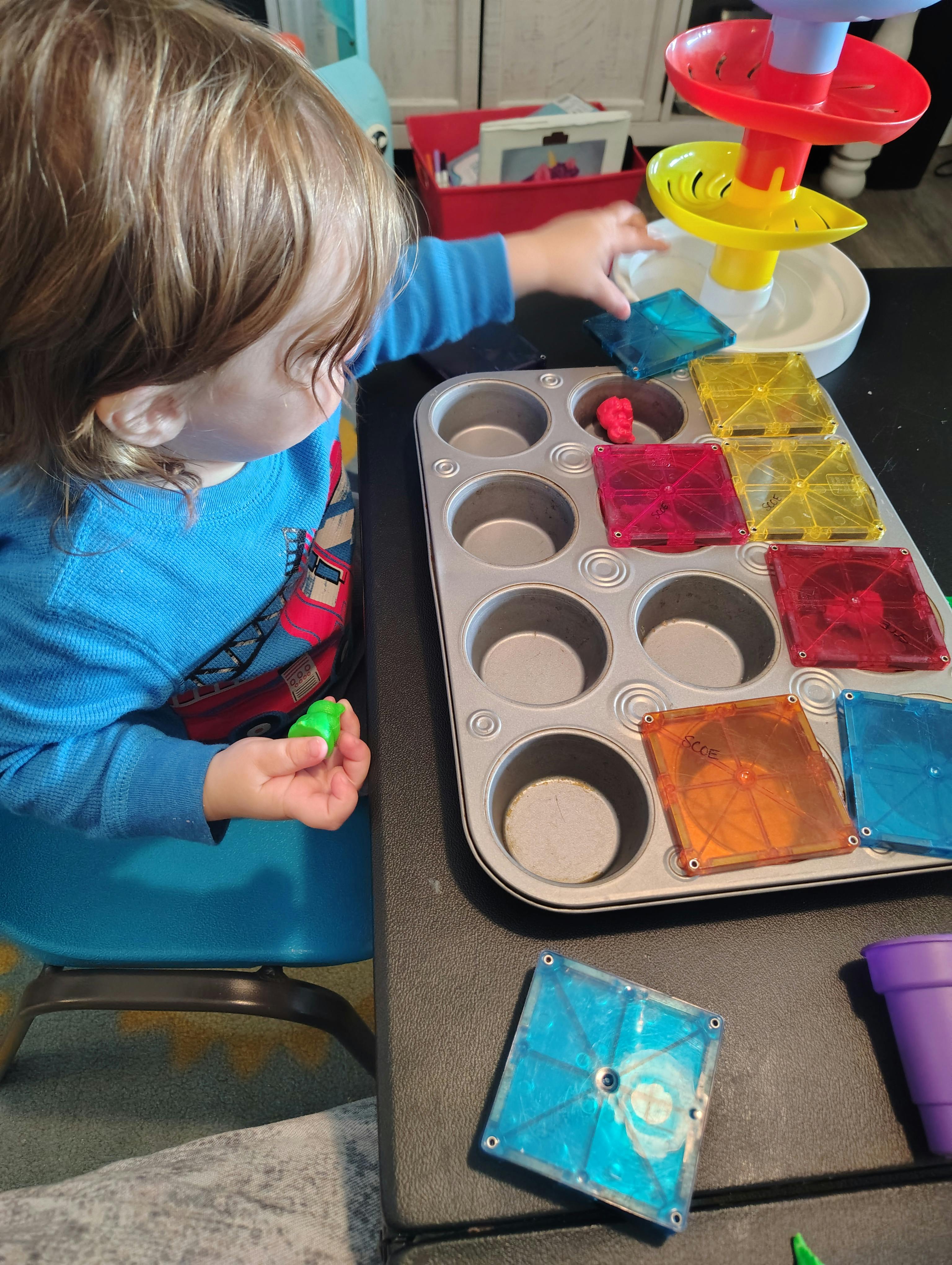 Child playing with colorful magnetic tiles and a muffin tin on a table