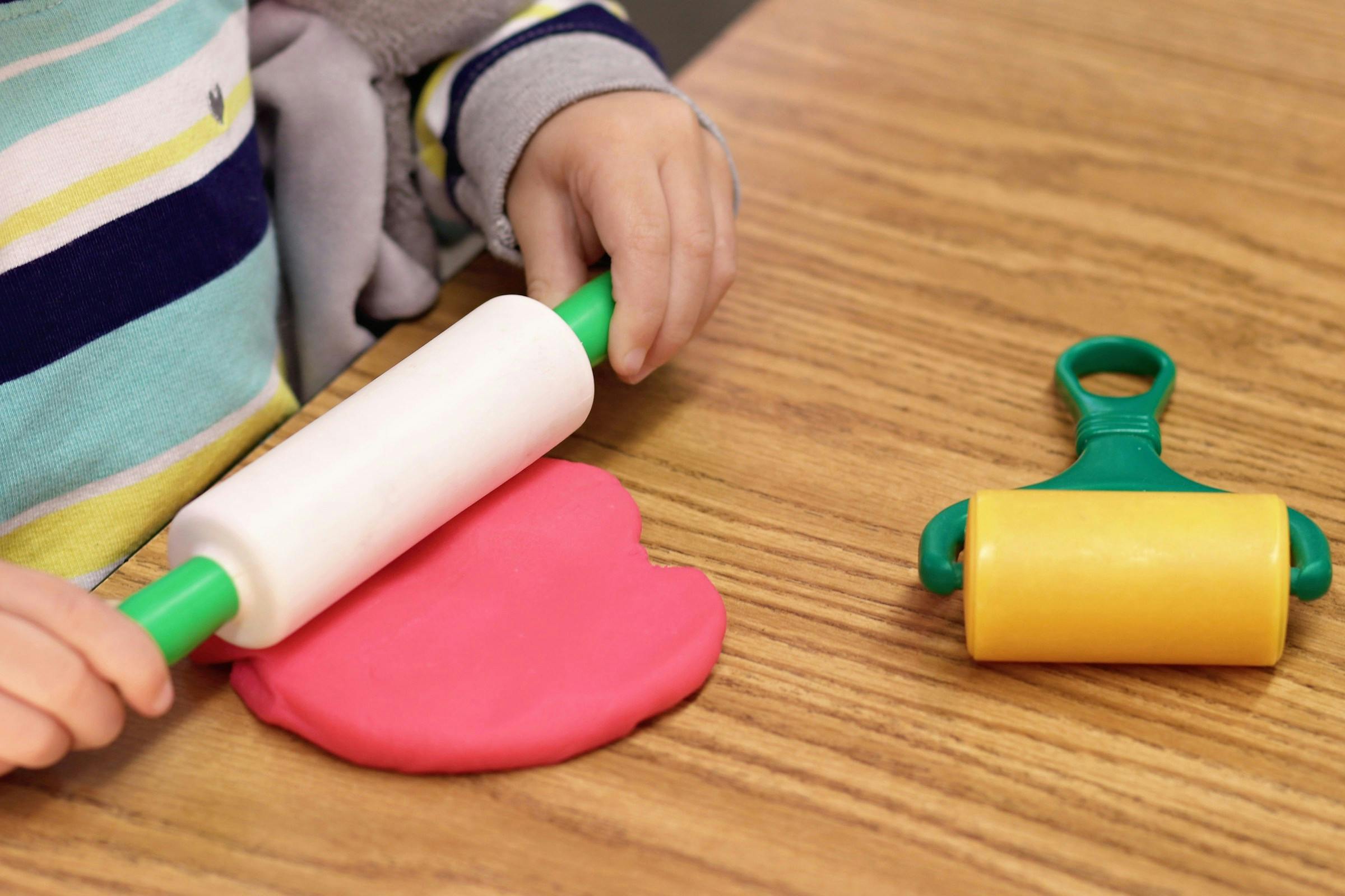Child using a rolling pin on pink playdough