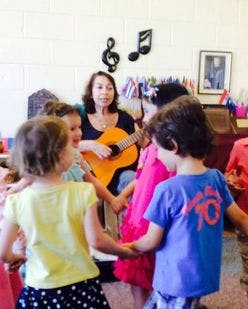 Adult playing guitar for children holding hands in a circle