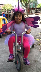 Child in unicorn costume riding a tricycle