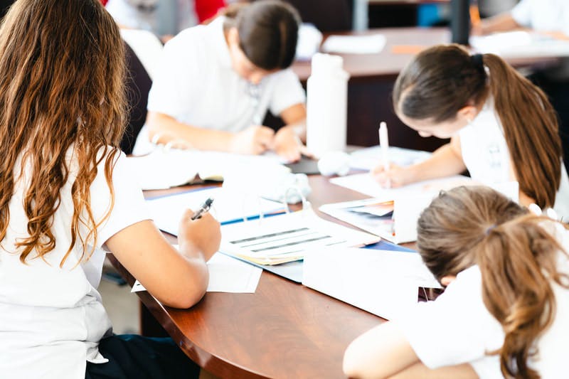 Children working on papers at a wooden table in a classroom