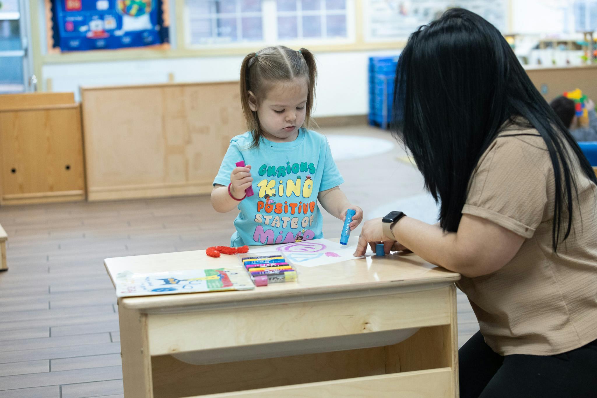 Child and person drawing at a small table in a classroom