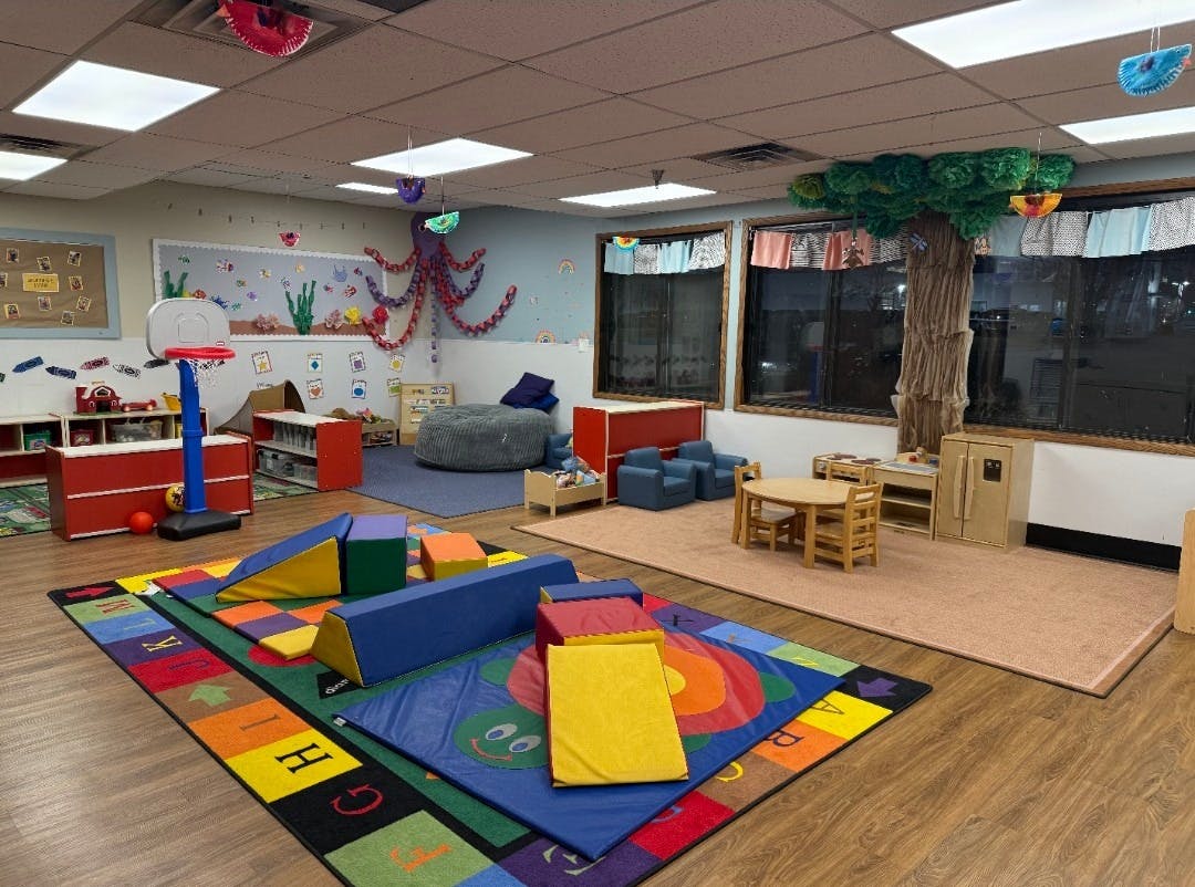 Colorful playroom with soft play equipment, small tables, and a basketball hoop
