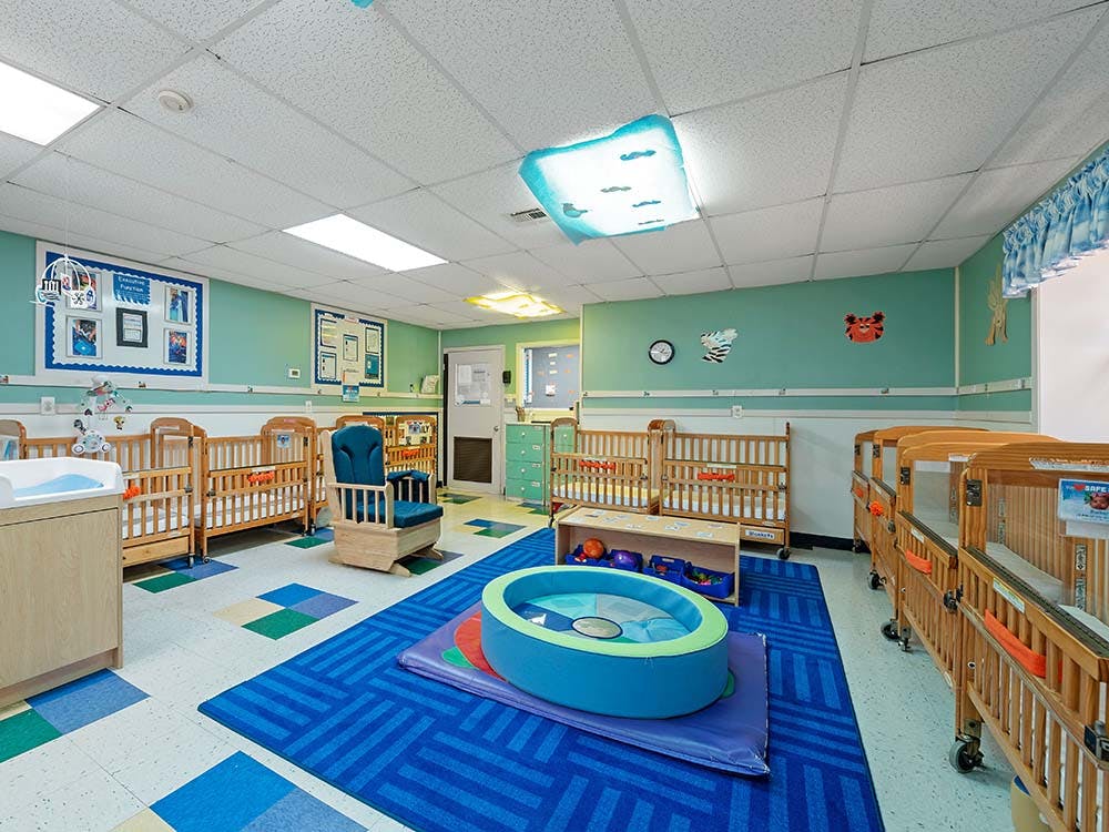 A room with several cribs, a rocking chair, and a blue rug with a play mat