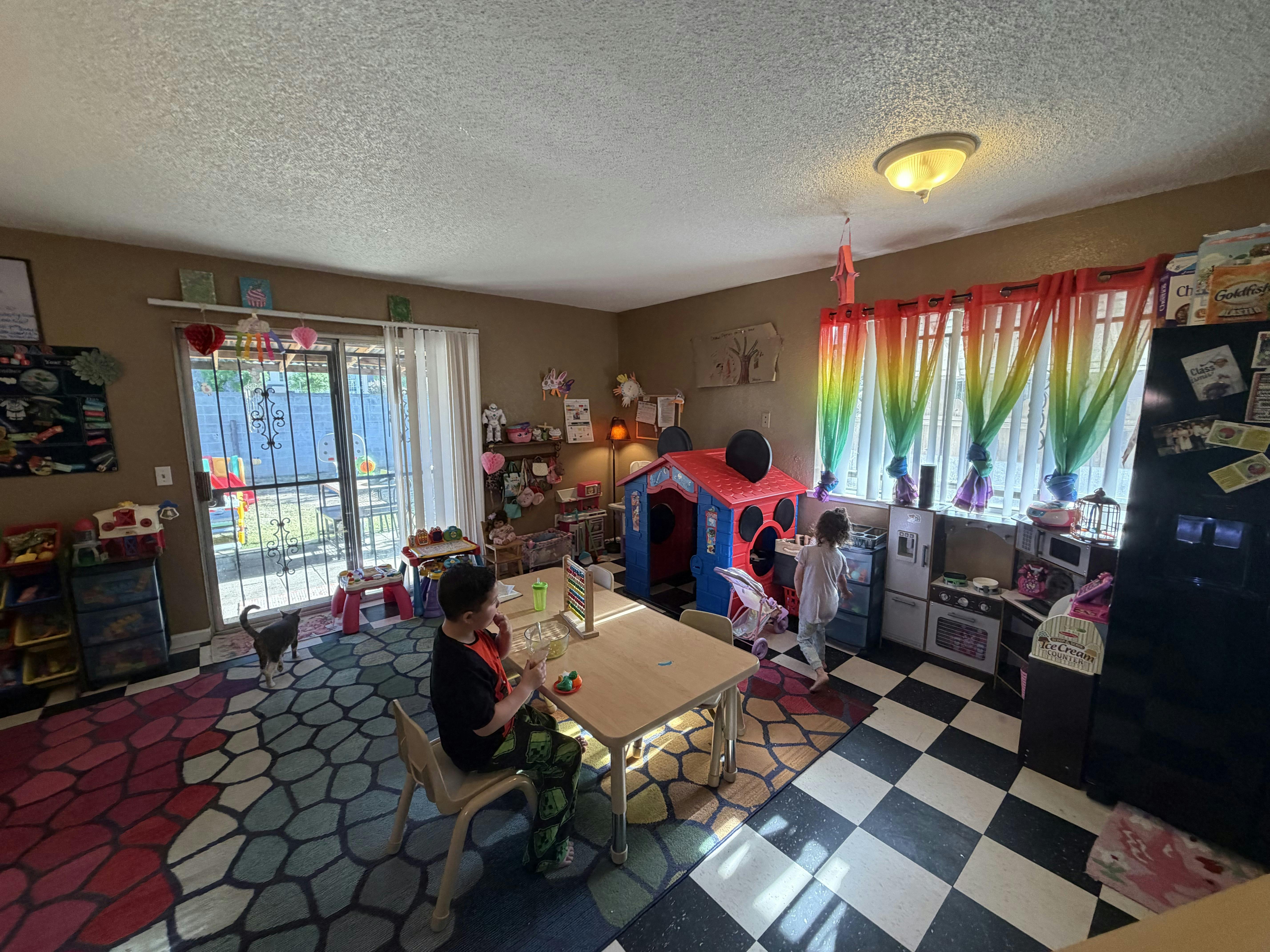 Children in a playroom, one at a table and another by a playhouse