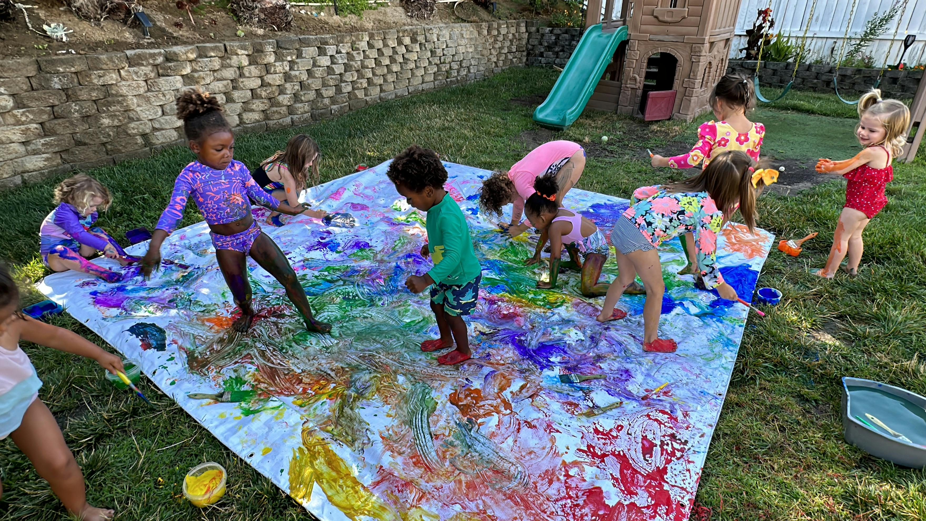 Children painting on a large white sheet outdoors