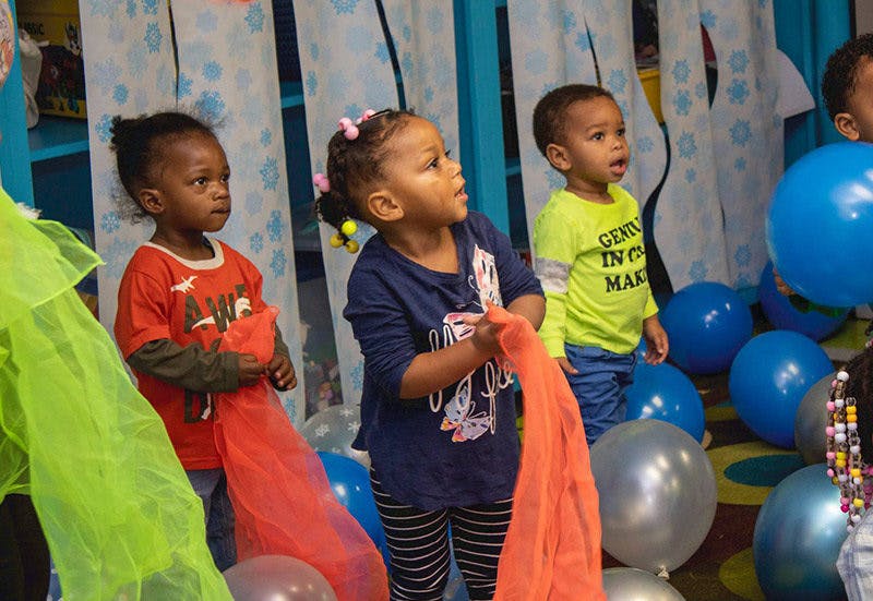 Three children holding colorful scarves among balloons