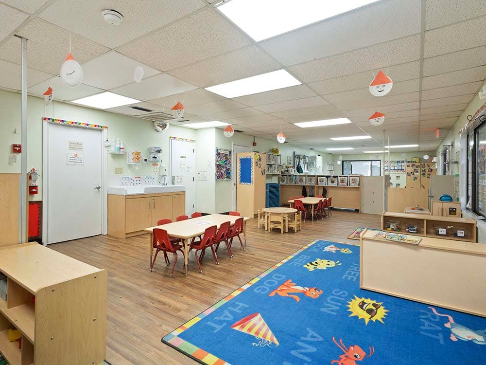 Empty preschool classroom with small tables and chairs and a colorful rug