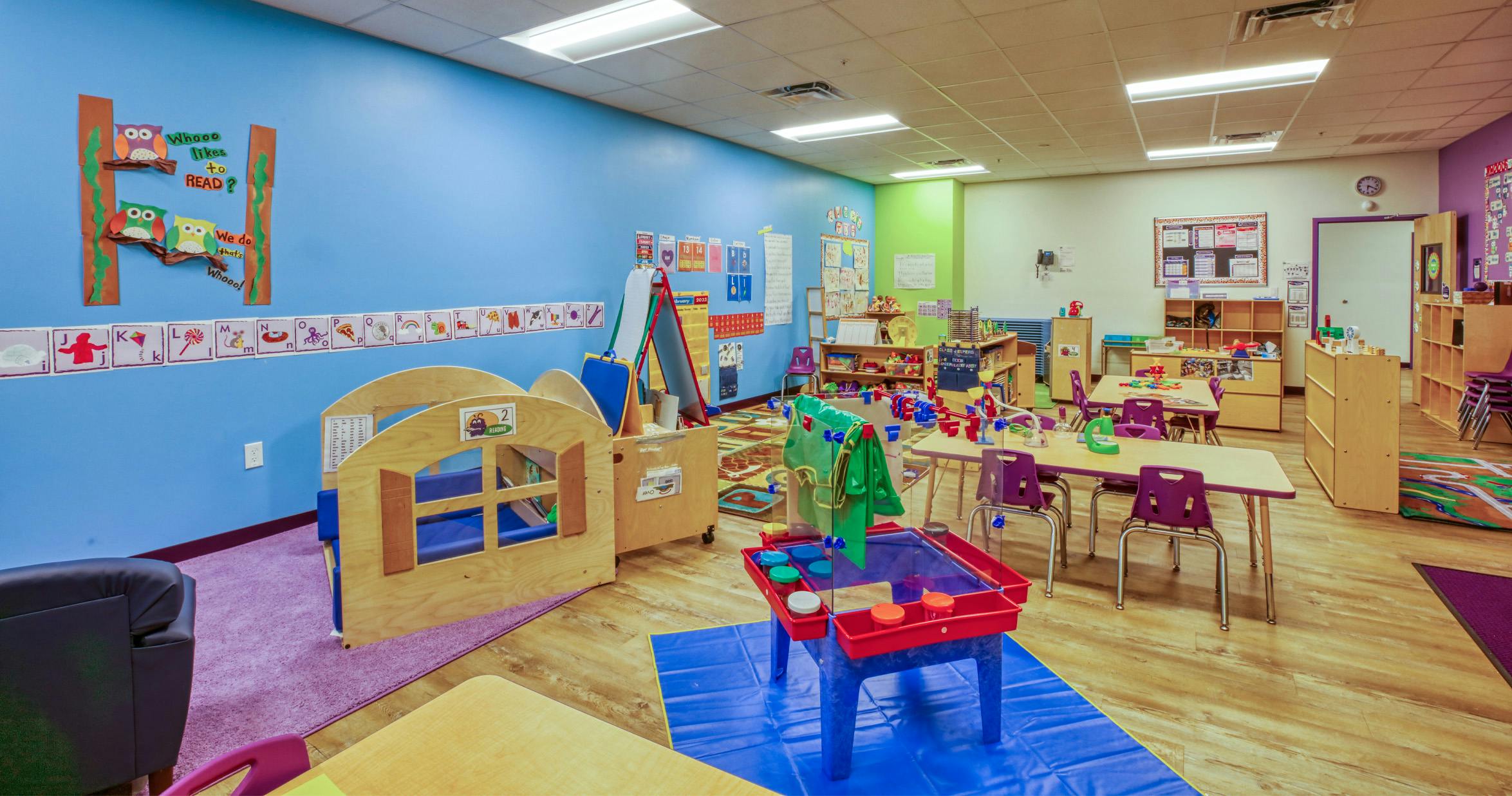 Colorful preschool classroom with tables, chairs, and play areas