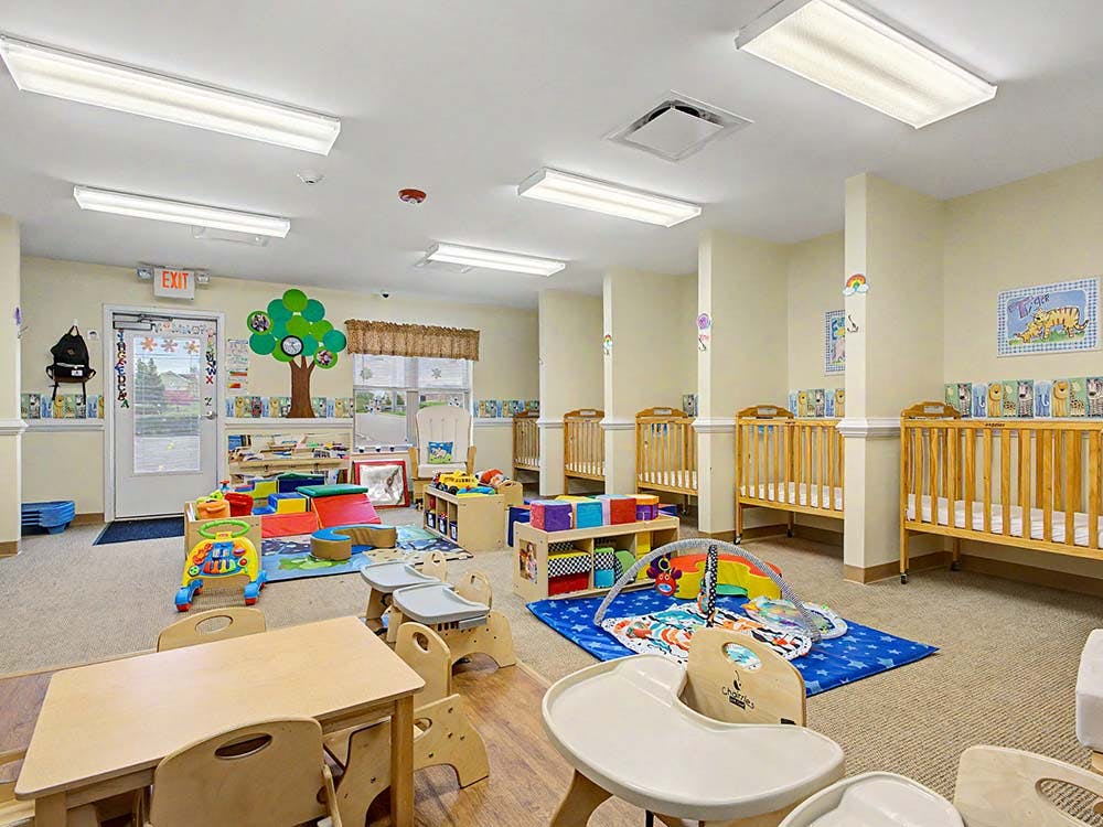 daycare classroom with multiple cribs, play mats, and small furniture