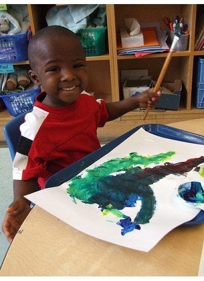 Child holding a paintbrush over a colorful painting