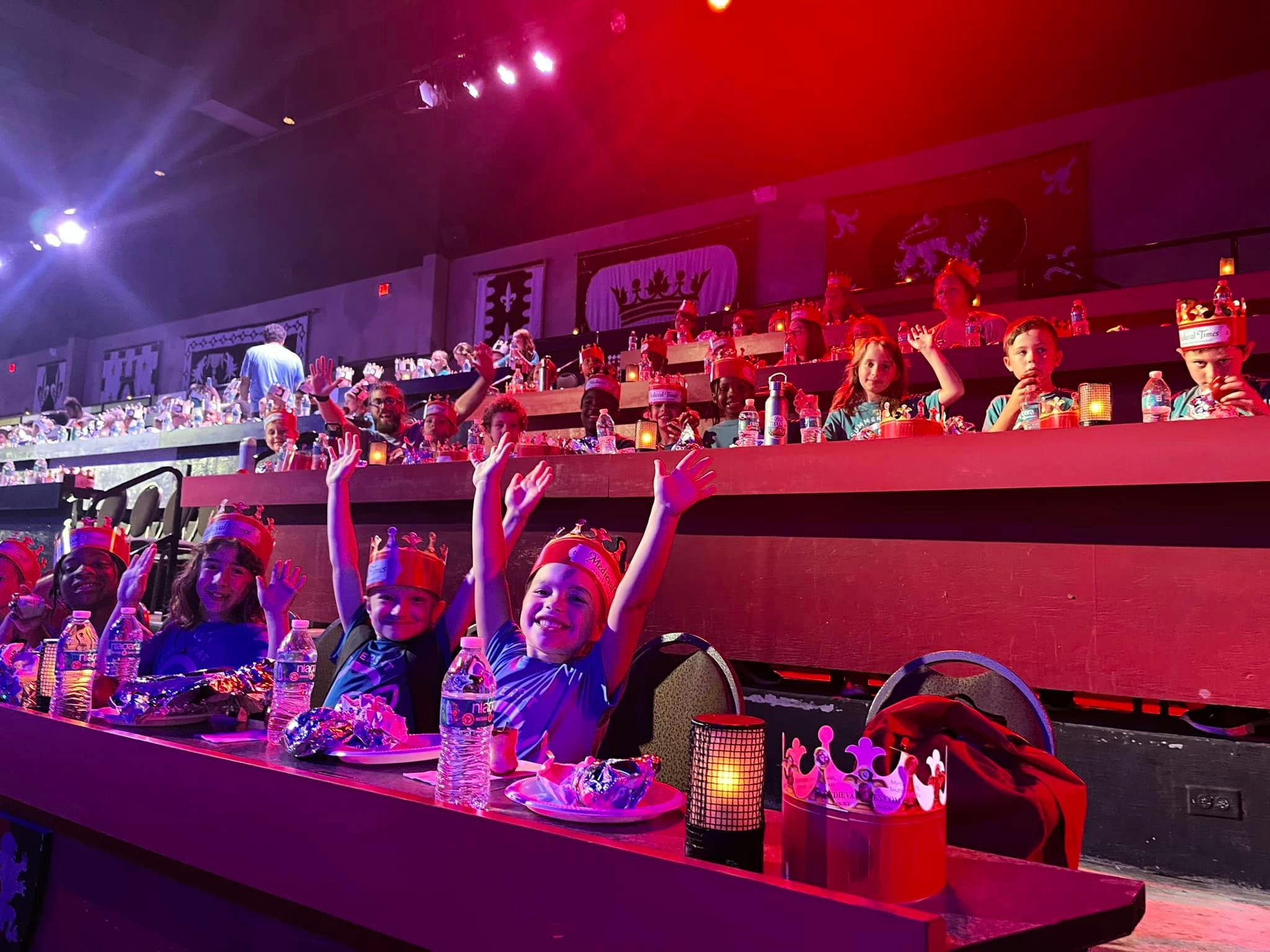 Children in paper crowns raising hands at a show