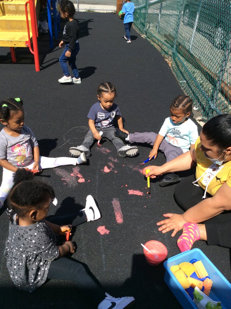 Adult and children sitting on ground drawing with chalk