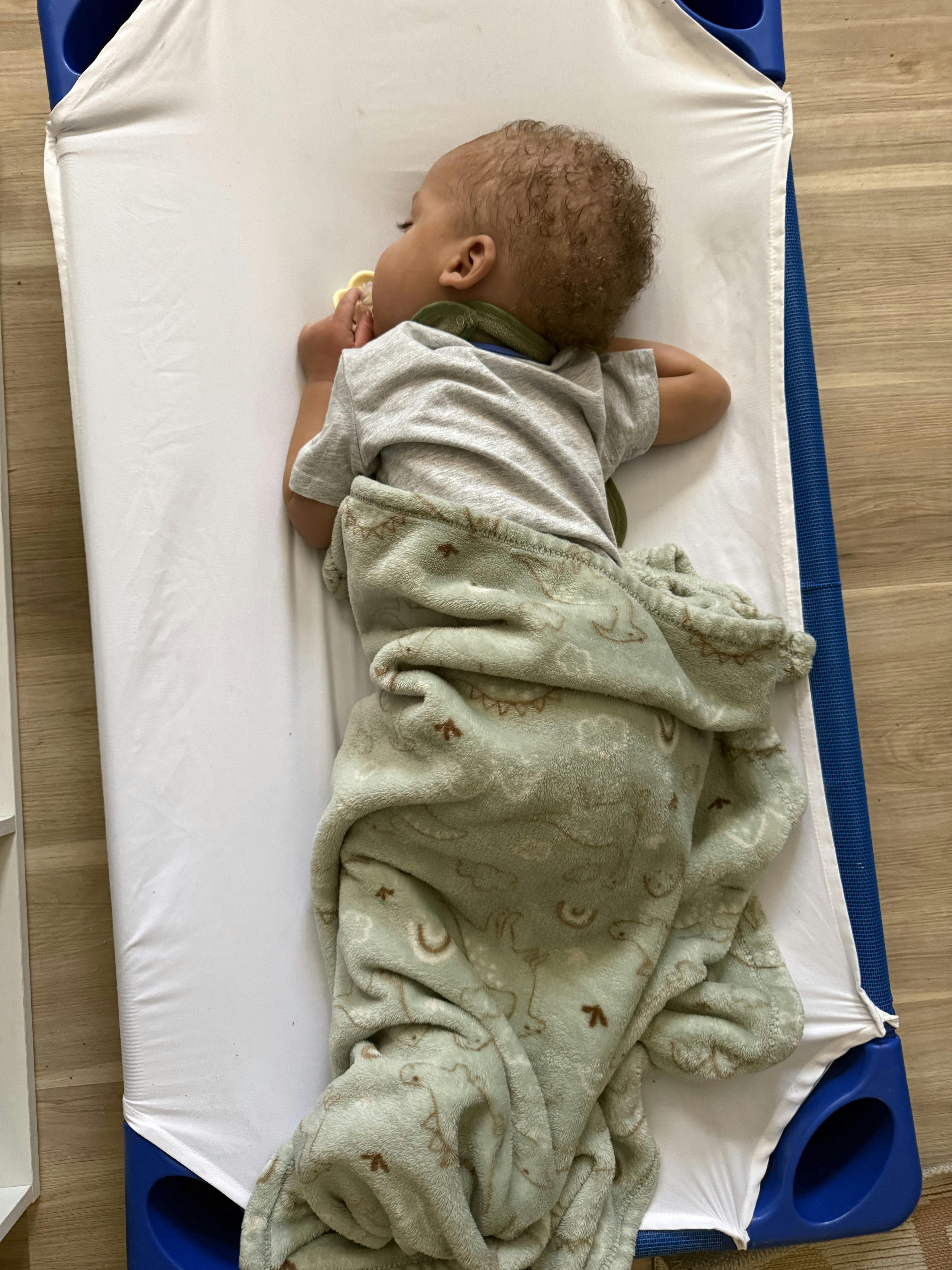Child sleeping on a cot with a green blanket