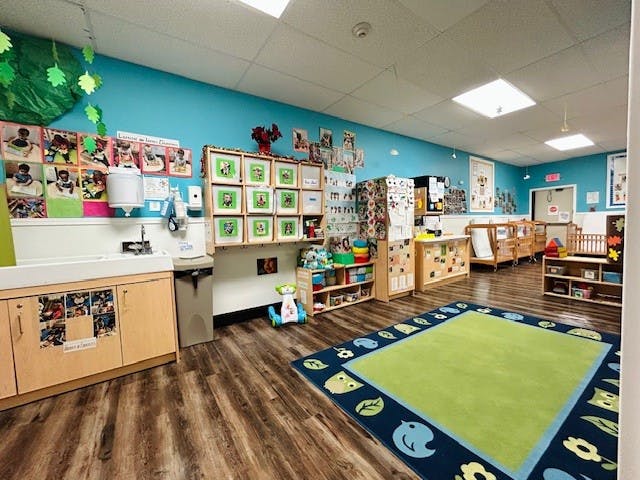 Classroom with changing table, cribs, colorful rug, and children's artwork