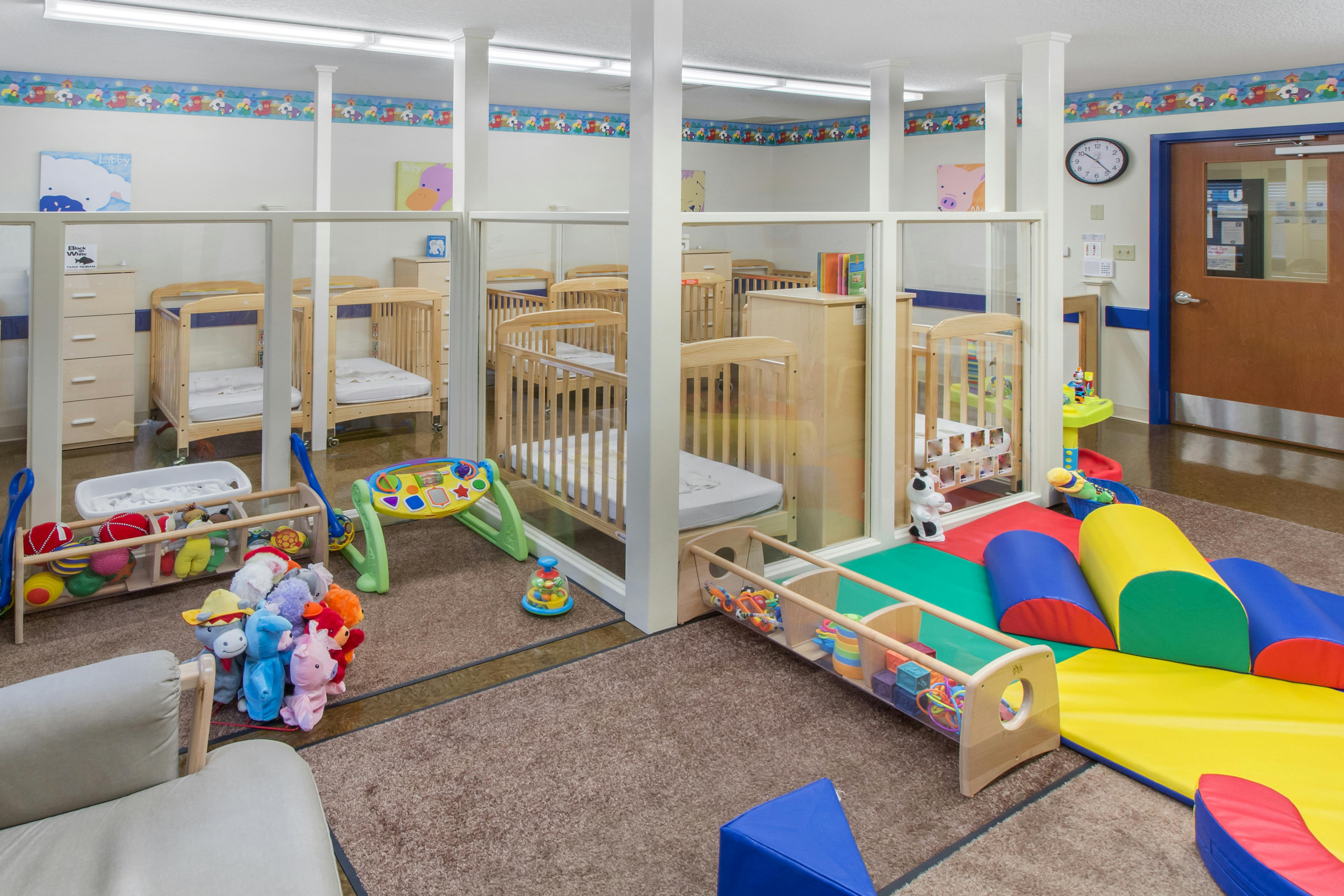 multiple wooden cribs separated by glass partitions in a daycare or nursery room