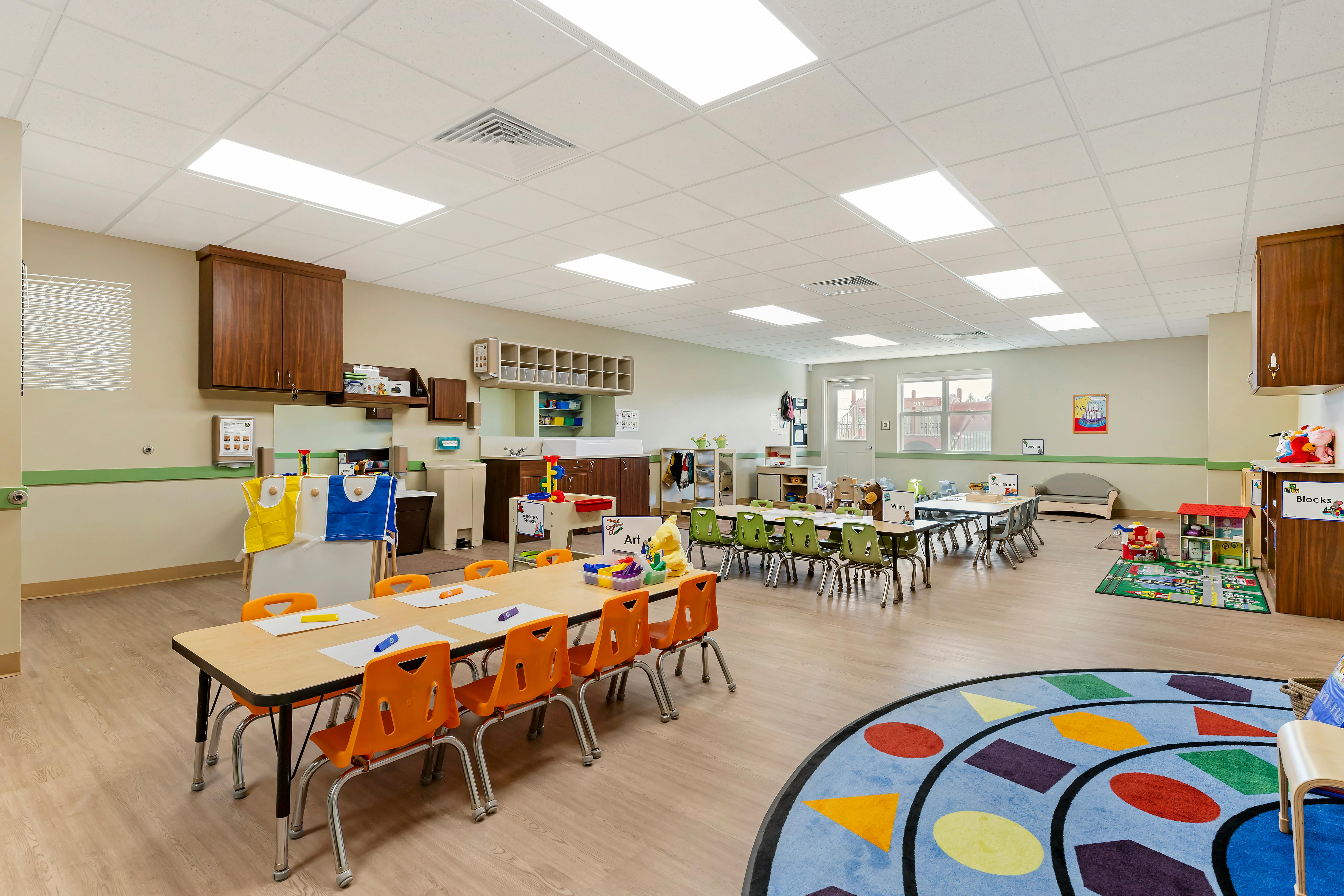 Classroom with child-sized tables and chairs, play mats, and learning stations