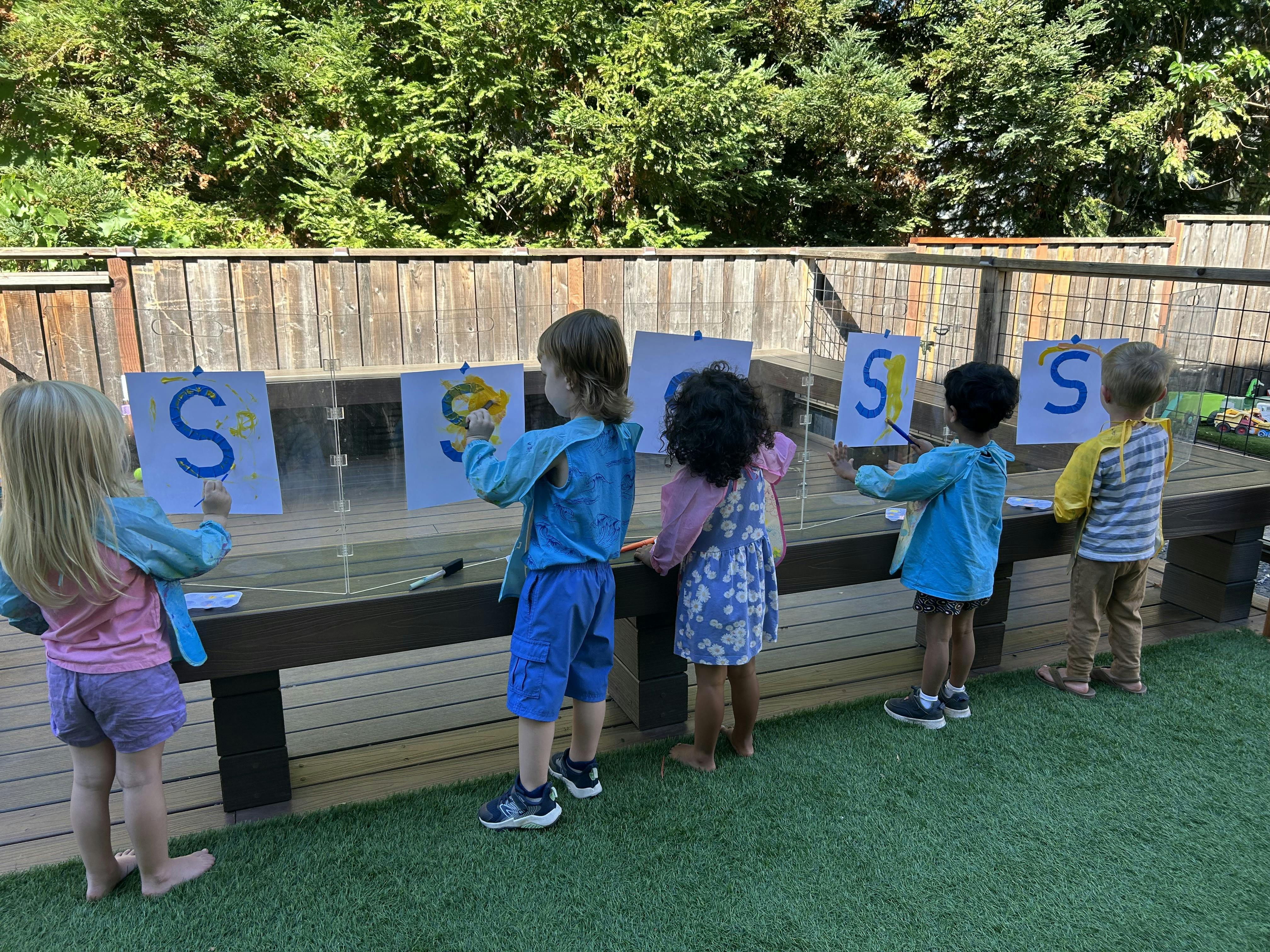 Children painting letters on easels outdoors