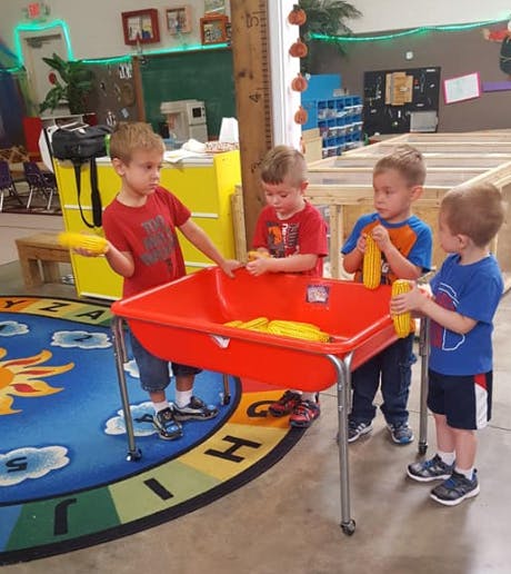 Four children playing with corn cobs in a red bin