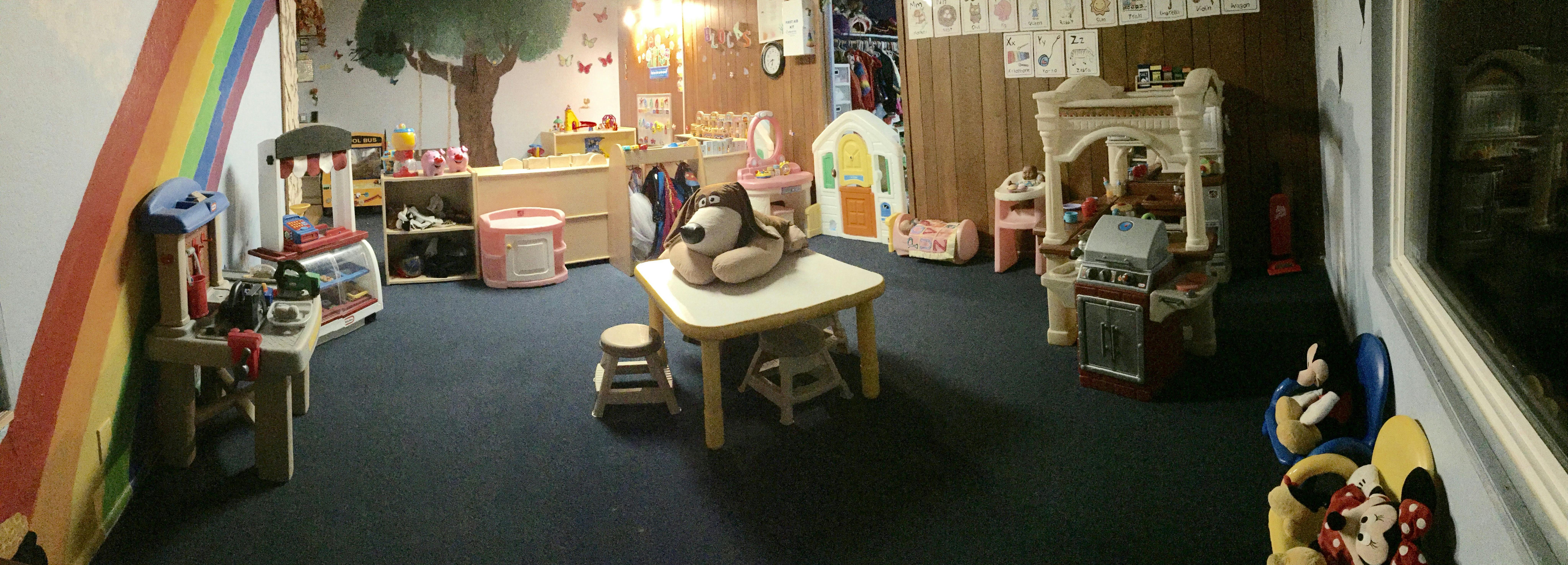 Playroom with small table and chairs, toy kitchen, and rainbow decoration