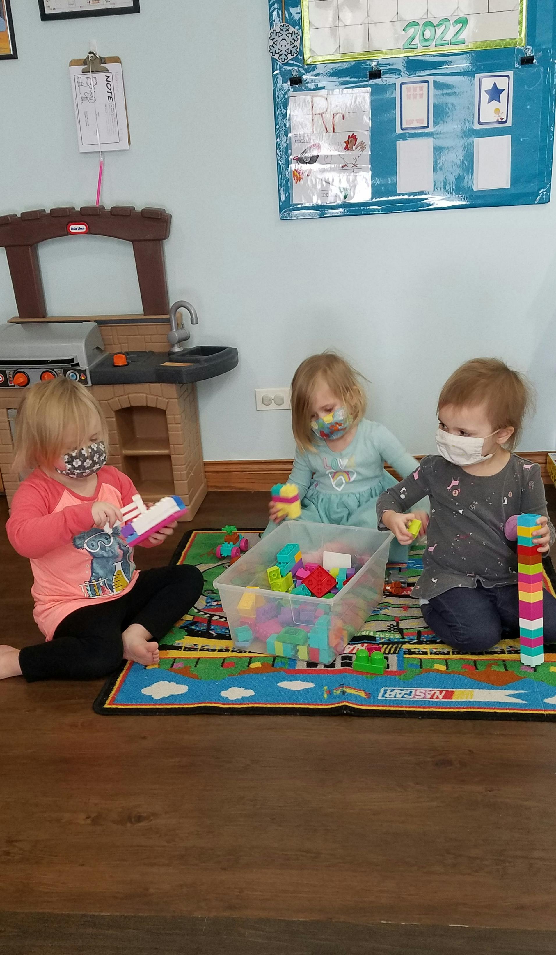 Three children playing with blocks on a mat in a classroom