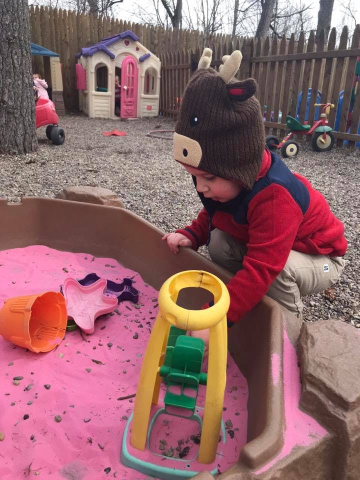 Child in a moose hat playing in a sandbox with pink sand