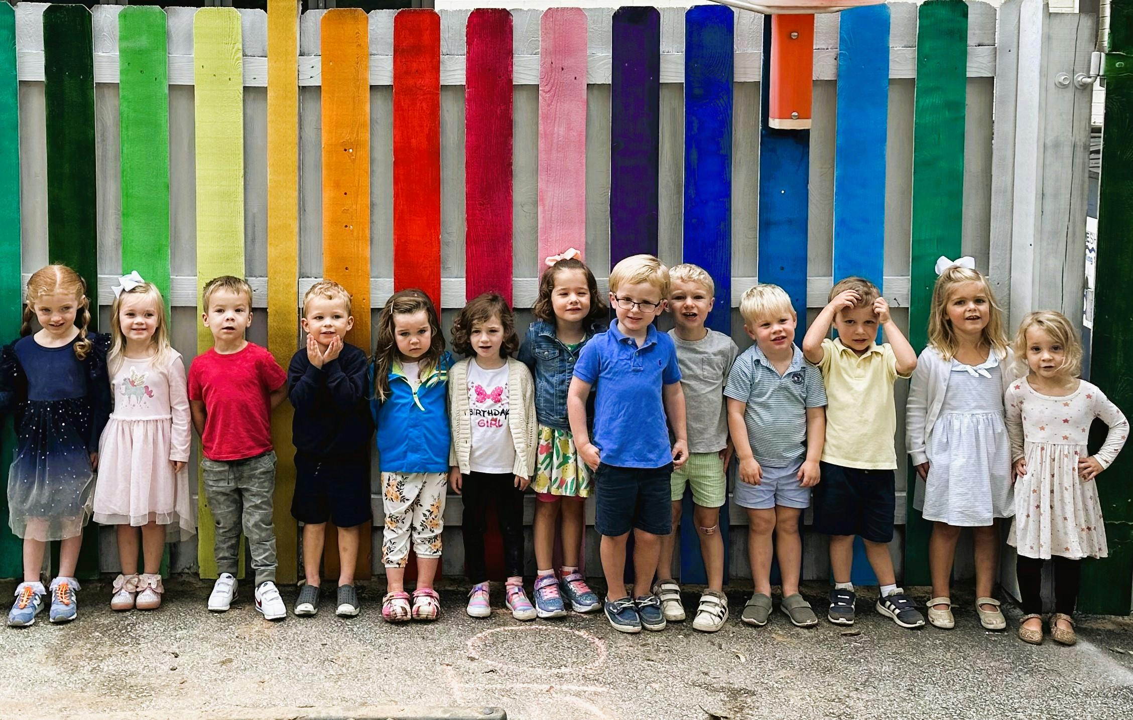 Group of children standing in front of a colorful fence