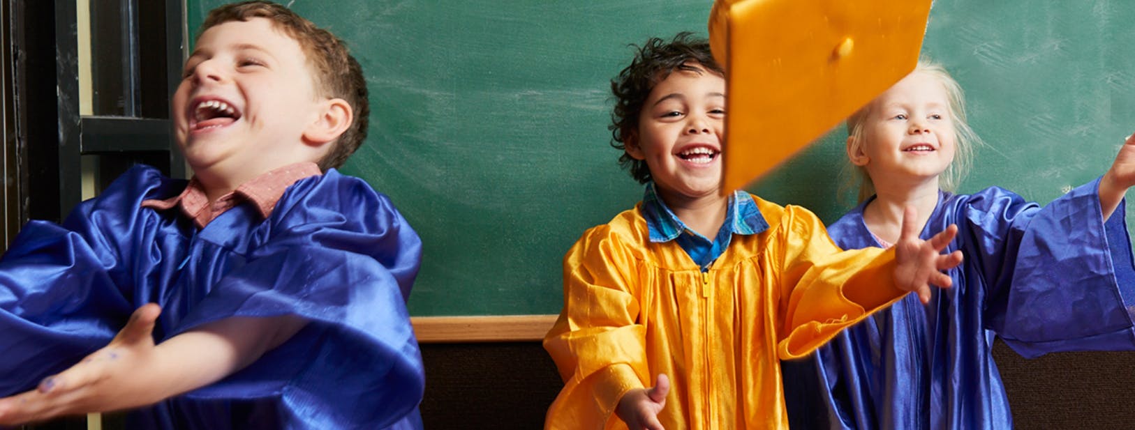 Three children in graduation gowns throwing a cap in the air