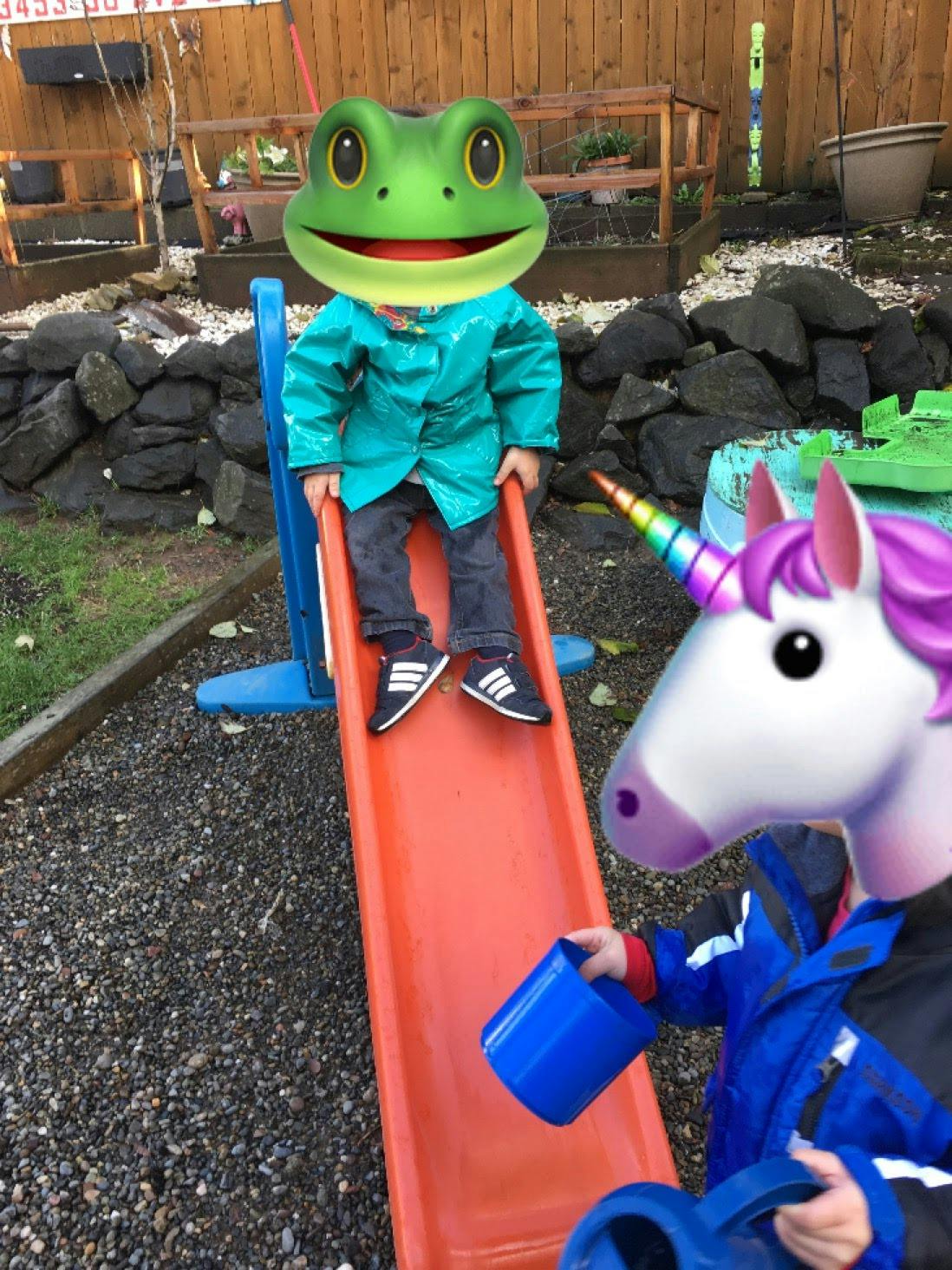 Child on a slide with another child holding a blue bucket