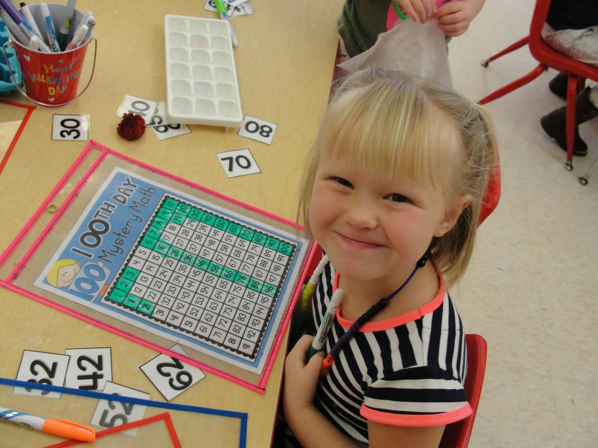 Child at a desk with a 100 chart and number cards