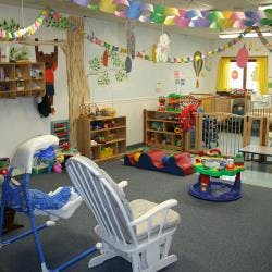 Childcare room with cribs, play mats, and a rocking chair