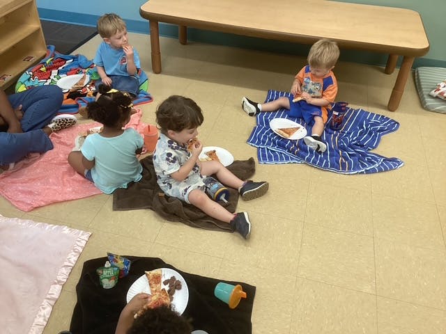 Group of children eating pizza on blankets in a classroom