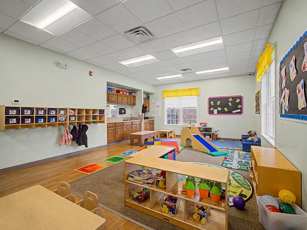 Empty children's classroom with cubbies, play slide, and activity rugs