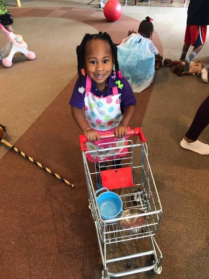 Child in an apron pushing a toy shopping cart