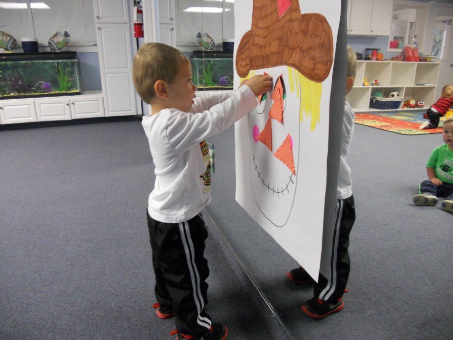 Child decorating a large paper pumpkin in a classroom