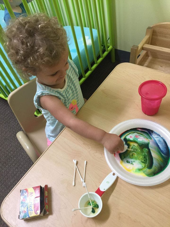 Child playing with colorful liquid in a bowl on a table