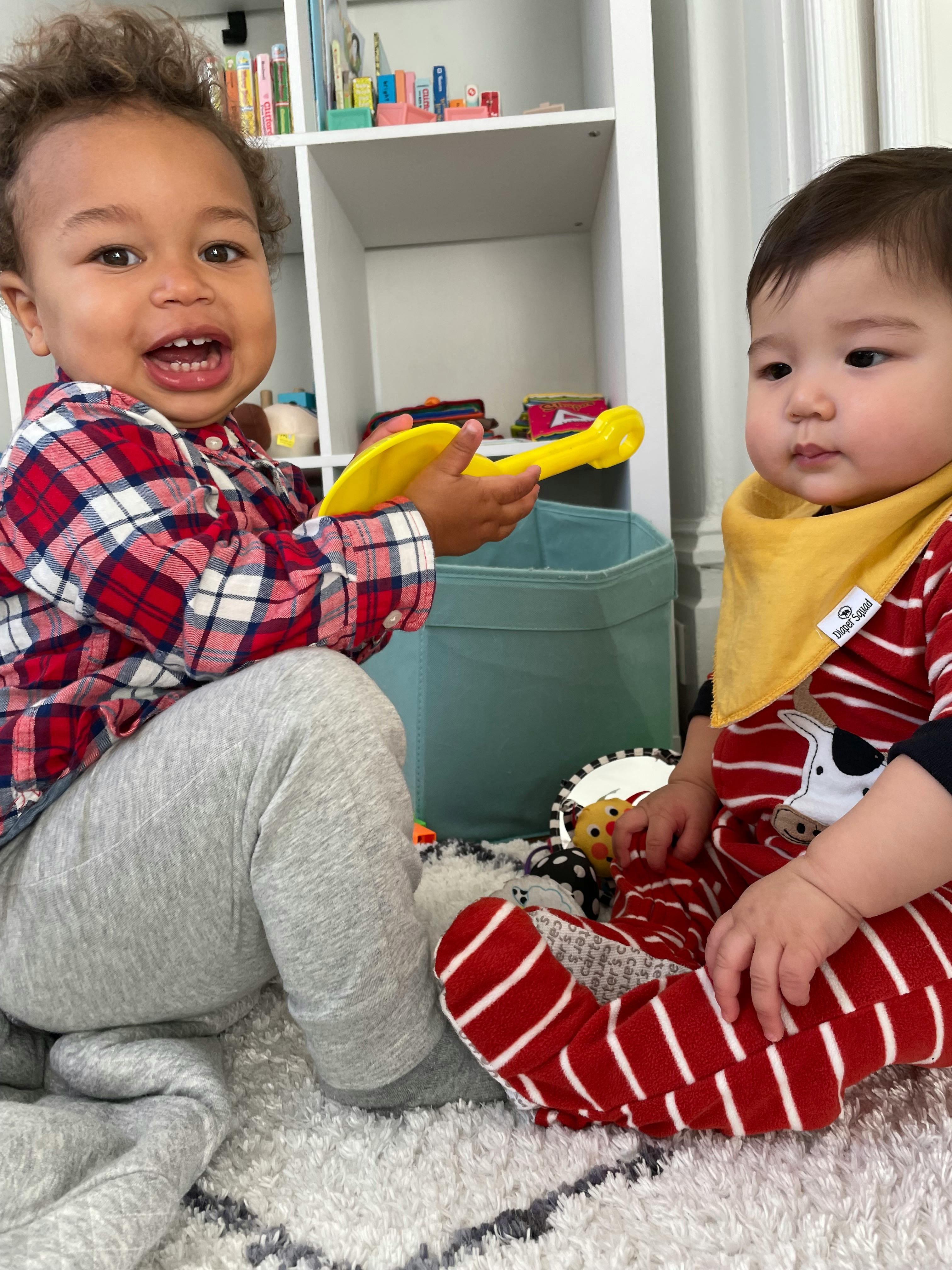 Two children playing with a toy on a rug near a shelf