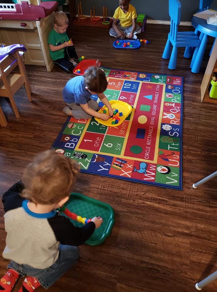 Three children playing with toys on a colorful alphabet and numbers rug