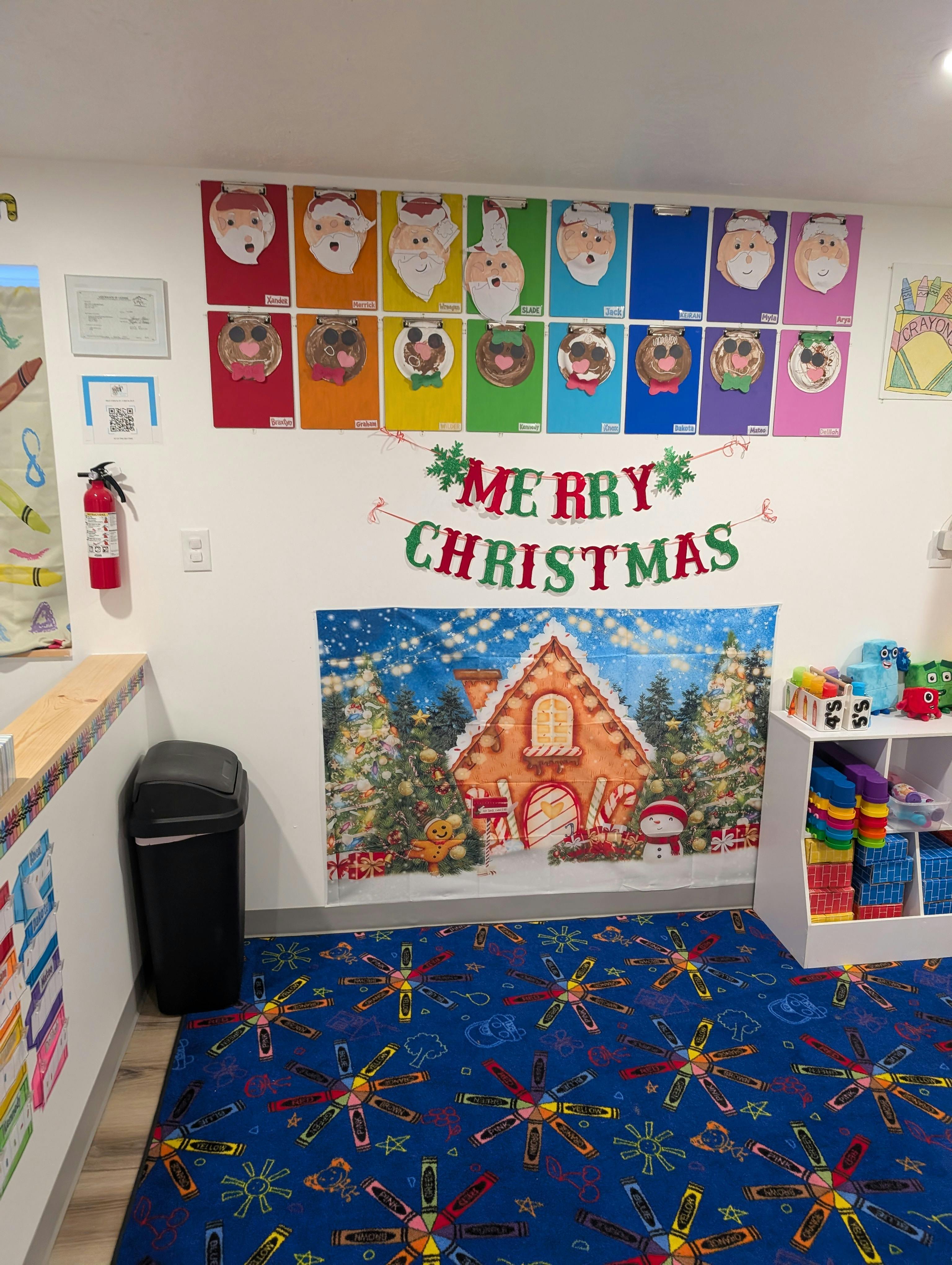 Classroom wall decorated with Santa faces, a Merry Christmas banner, and a gingerbread house