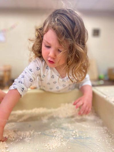 Child playing with sand in a sensory bin