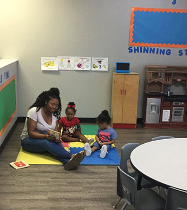 Person reading to two children in a classroom