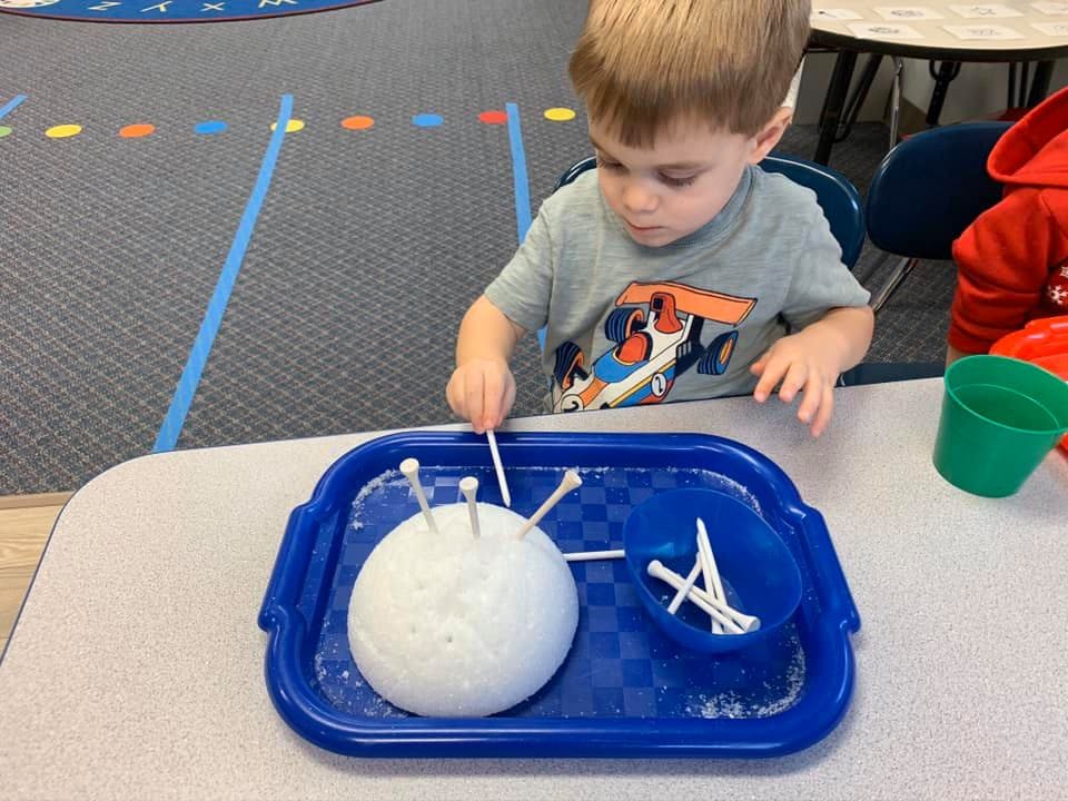 Child placing golf tees into a white foam ball on a blue tray