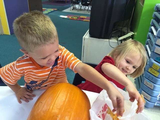 Two children with a pumpkin, one reaching into a bag